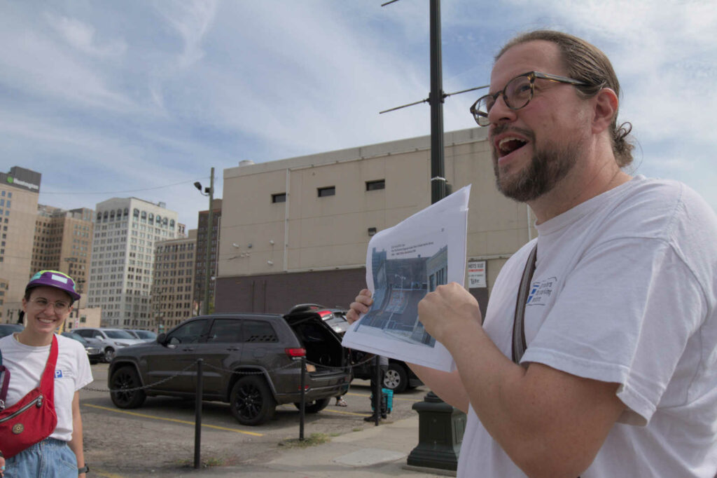 Francis Grunow of Detroiters for Parking Reform stands near Cass Avenue and Columbia Streets showing a photograph of the former Chin Tiki, demolished in the 2000s for surface parking.