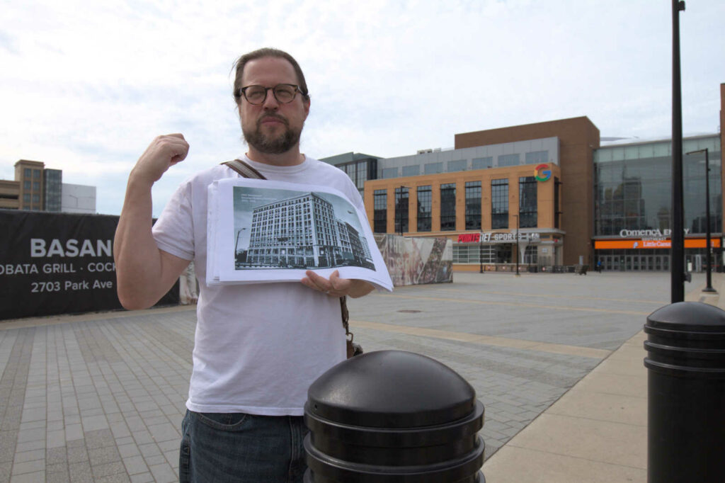 Francis Grunow holds up a historic photo of the Donovan Building, formerly Motown Records headquarters, at the site of a plaza and abandoned construction site in the District Detroit.